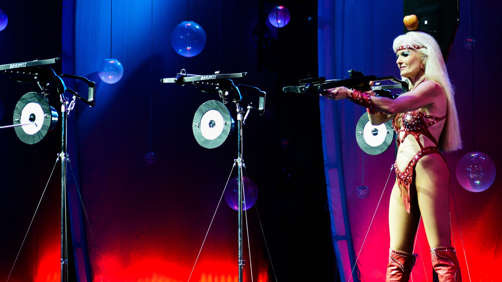 Female performer aiming crossbow at targets on stage at WOW The Vegas Spectacular