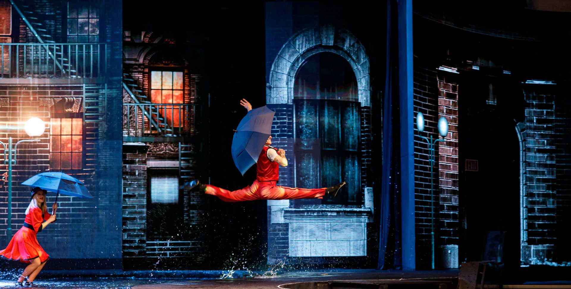 Dancer leaping with umbrella on stage with 3D projections and water effects at WOW Las Vegas